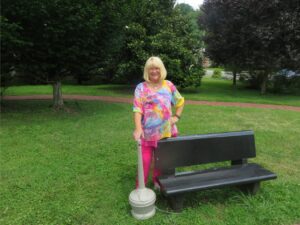 Lady with cigarette butt receptacle near park bench