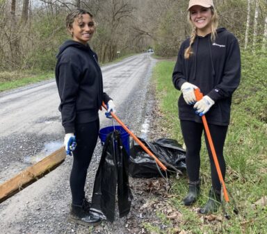 Two girls and a dog picking up litter along a road.