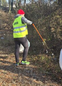 Person wearing a safety vest using a litter grabber to pick up trash at a local park in Richmond.