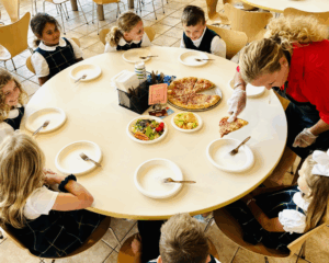 Students at lunch table being served by an adult, using compostable plates and forks.
