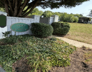 Photo of entrance way to Courts of St. Francis neighborhood with wooden sign and landscaping in need of renovation