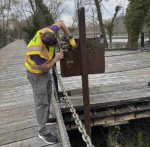 Photo of a volunteer scraping off graffiti and stickers from a sign on the Mount Vernon Trail