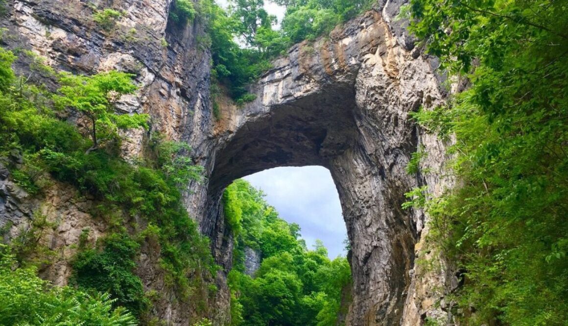Photo of natural rock bridge with blue skies and trees, located in Natural Bridge State Park, Virginia